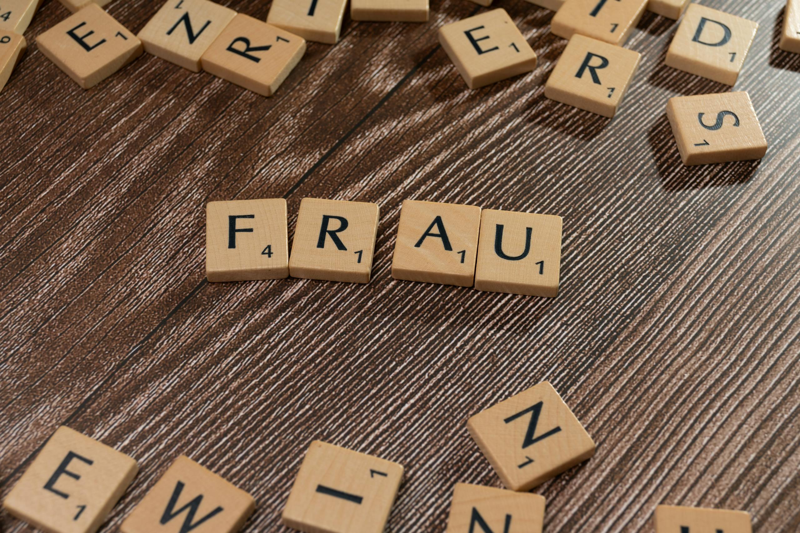 Scrabble-like tiles spelling 'Frau' on a textured wooden surface, suggestive of gender topics.